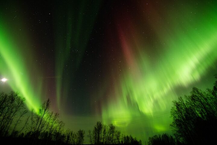 Illustrative aurora borealis (northern lights) glowing over a dark northern horizon under clear skies.