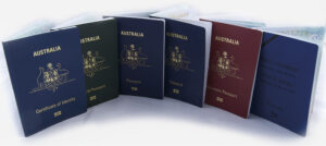 Row of Australian P-Series passports (blue, red, green, and maroon covers) standing upright on a white background.