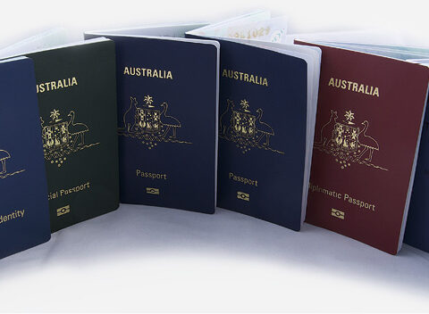 Row of Australian P-Series passports (blue, red, green, and maroon covers) standing upright on a white background.