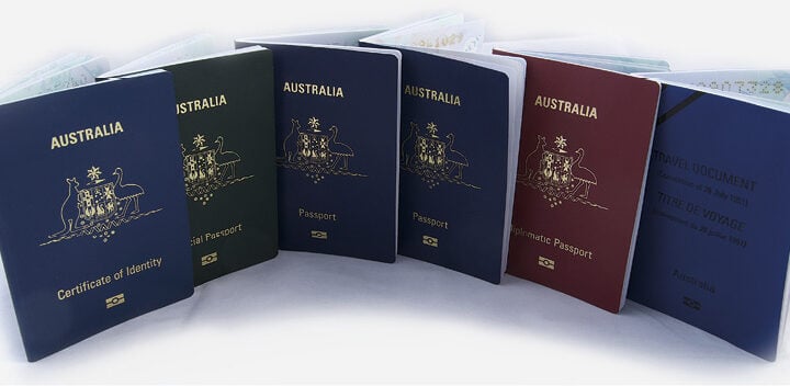 Row of Australian P-Series passports (blue, red, green, and maroon covers) standing upright on a white background.