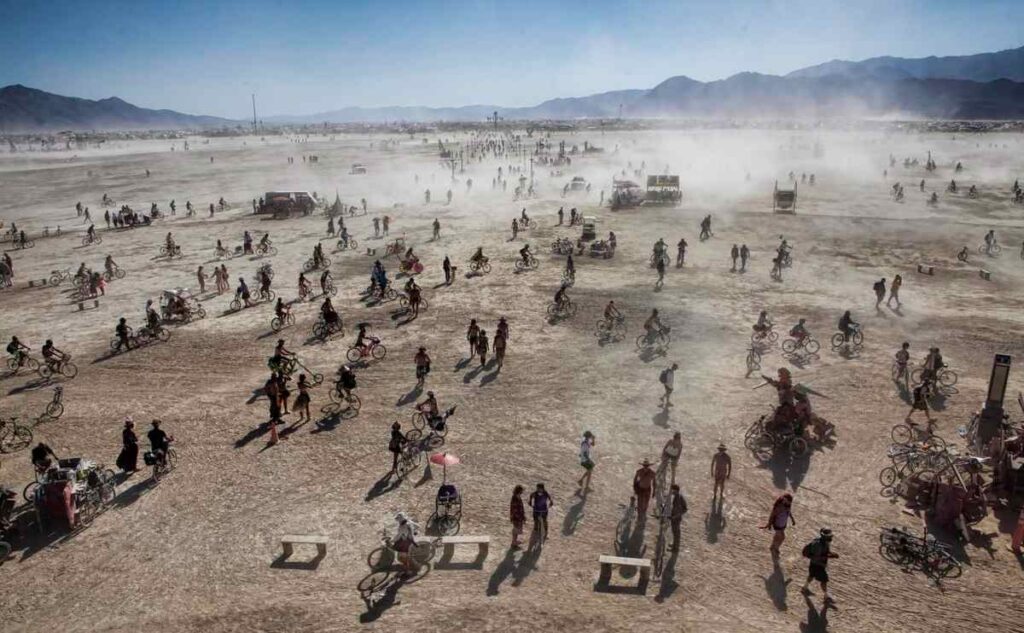 Aerial panoramic view of Burning Man 2010 festival showing geometric layout of camps and art installations in Black Rock Desert under hazy dust-filled skies.