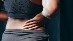 Person in athletic wear holding their lower back in pain, shown from behind with focus on the torso and hand placement indicating back discomfort.
