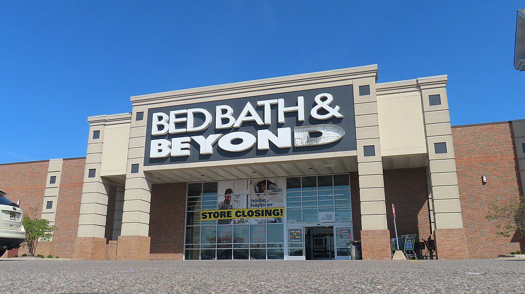 Exterior of a closed Bed Bath & Beyond store in Taylor, Michigan, showing the company's blue and white signage on a brick building façade.