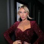 Billie Shepherd in a sparkly deep red long‑sleeve dress with a plunging neckline in a dim hallway