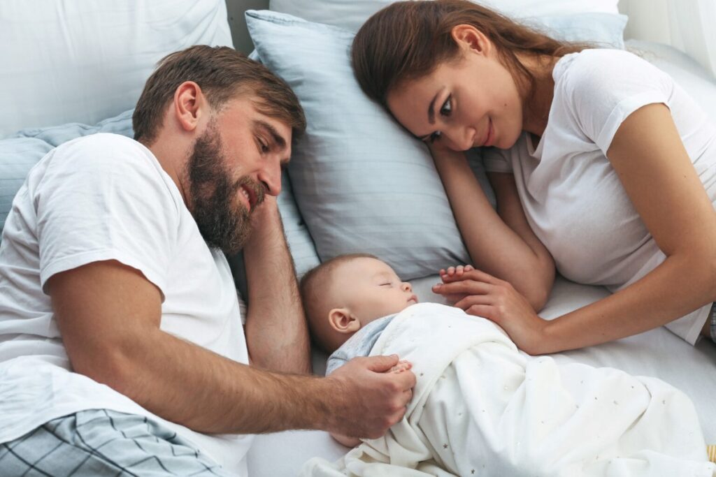 Mother and father lying in bed beside their baby, illustrating parental bonding and nighttime caregiving responses.