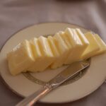 Slices of European-style butter arranged on a plate beside a butter knife.