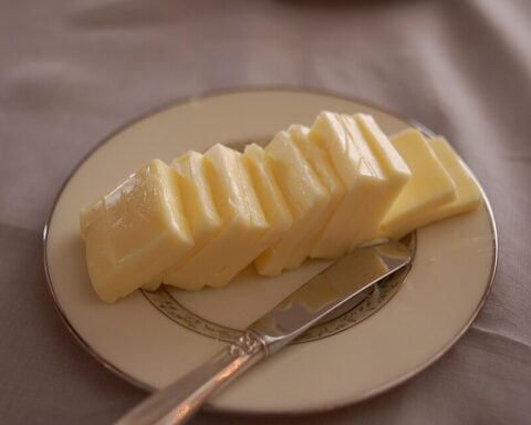 Slices of European-style butter arranged on a plate beside a butter knife.