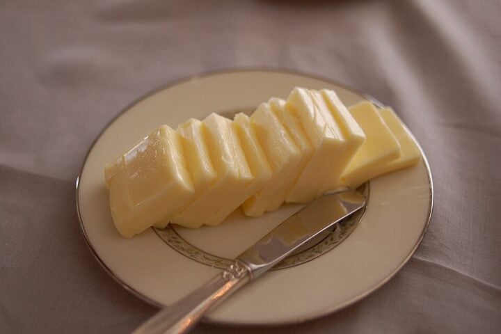 Slices of European-style butter arranged on a plate beside a butter knife.