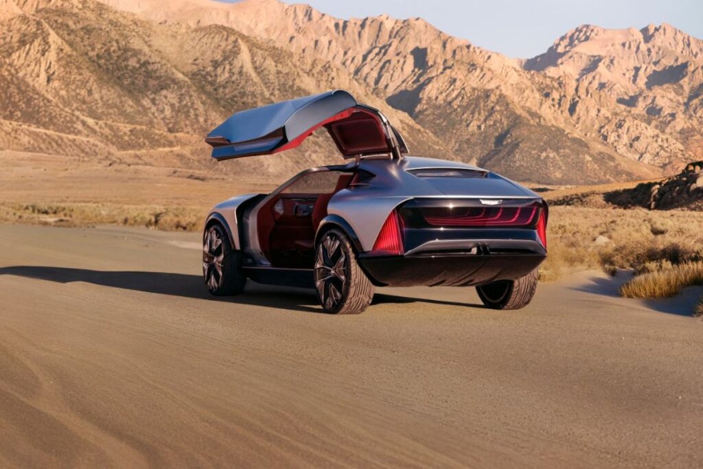 Rear view of the silver-blue Cadillac Elevated Velocity concept car with its gull-wing door open, set against a desert mountain landscape.