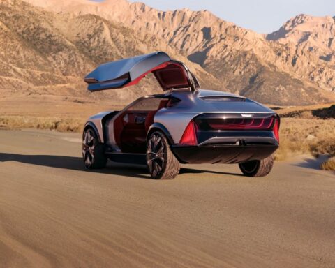 Rear view of the silver-blue Cadillac Elevated Velocity concept car with its gull-wing door open, set against a desert mountain landscape.