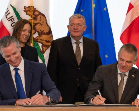 Governor Gavin Newsom and Danish Foreign Minister Lars Løkke Rasmussen signing the California-Denmark climate partnership agreement with officials observing in the background, including California Lieutenant Governor Eleni Kounalakis.