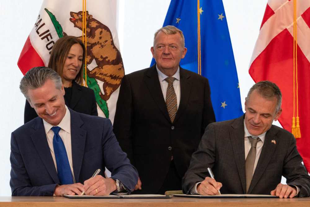 Governor Gavin Newsom and Danish Foreign Minister Lars Løkke Rasmussen signing the California-Denmark climate partnership agreement with officials observing in the background, including California Lieutenant Governor Eleni Kounalakis.