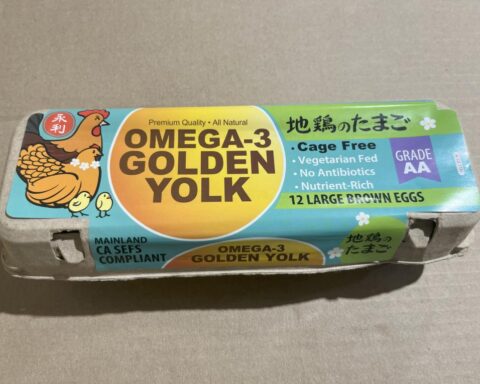 Carton of 12 large brown Omega-3 Golden Yolk eggs with colorful packaging featuring a chicken illustration, labeled as cage-free, vegetarian-fed, antibiotic-free, and Grade AA.