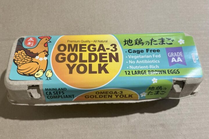 Carton of 12 large brown Omega-3 Golden Yolk eggs with colorful packaging featuring a chicken illustration, labeled as cage-free, vegetarian-fed, antibiotic-free, and Grade AA.