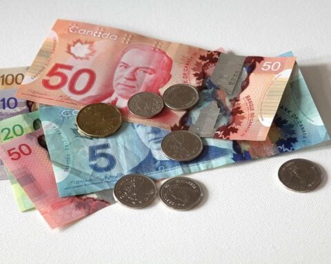 Canadian currency including $5, $10, $20, and $50 bills with several coins scattered on a white surface, illustrating Canada's economic situation as inflation rates fluctuate across different sectors