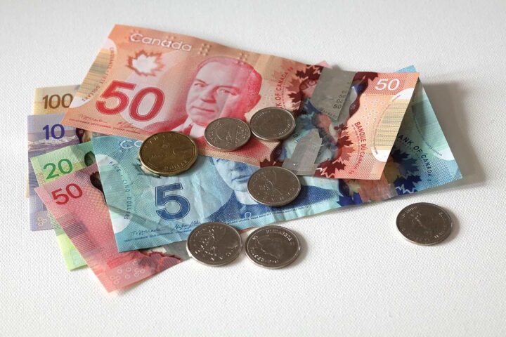 Canadian currency including $5, $10, $20, and $50 bills with several coins scattered on a white surface, illustrating Canada's economic situation as inflation rates fluctuate across different sectors