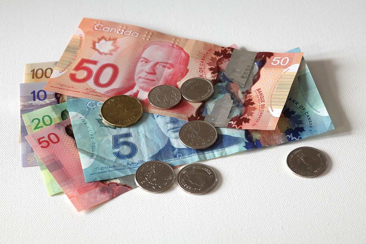 Canadian currency including $5, $10, $20, and $50 bills with several coins scattered on a white surface, illustrating Canada's economic situation as inflation rates fluctuate across different sectors