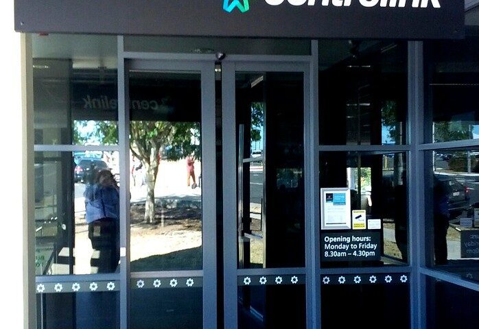 Entrance to a Centrelink service centre with glass doors and signage, representing Australian Government social security services.