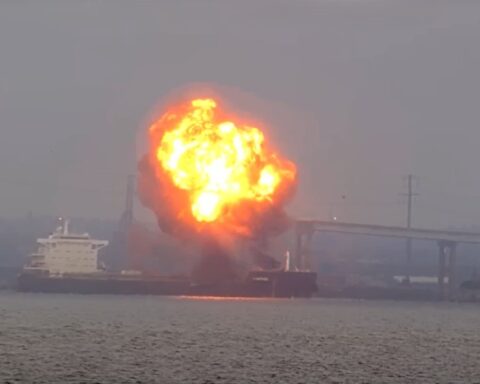 Flames and thick smoke billow from the bow of the W Sapphire bulk carrier near the Francis Scott Key Bridge as emergency vessels respond on Baltimore’s Patapsco River at dusk.