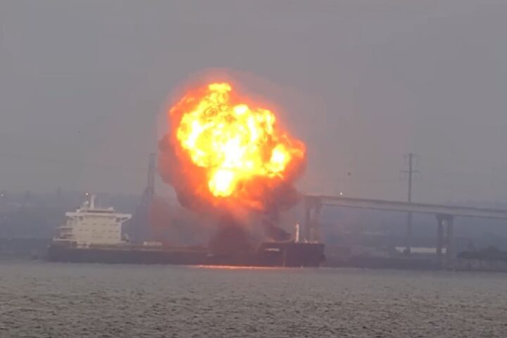 Flames and thick smoke billow from the bow of the W Sapphire bulk carrier near the Francis Scott Key Bridge as emergency vessels respond on Baltimore’s Patapsco River at dusk.