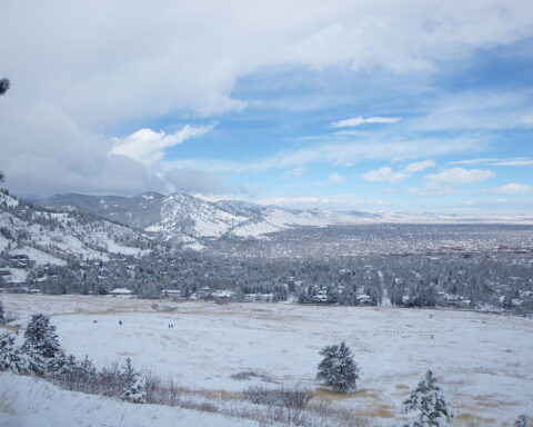 Snow-covered Boulder landscape with mountains and trees under a partly cloudy sky