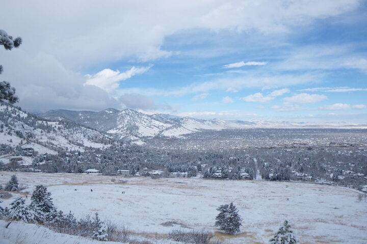Snow-covered Boulder landscape with mountains and trees under a partly cloudy sky