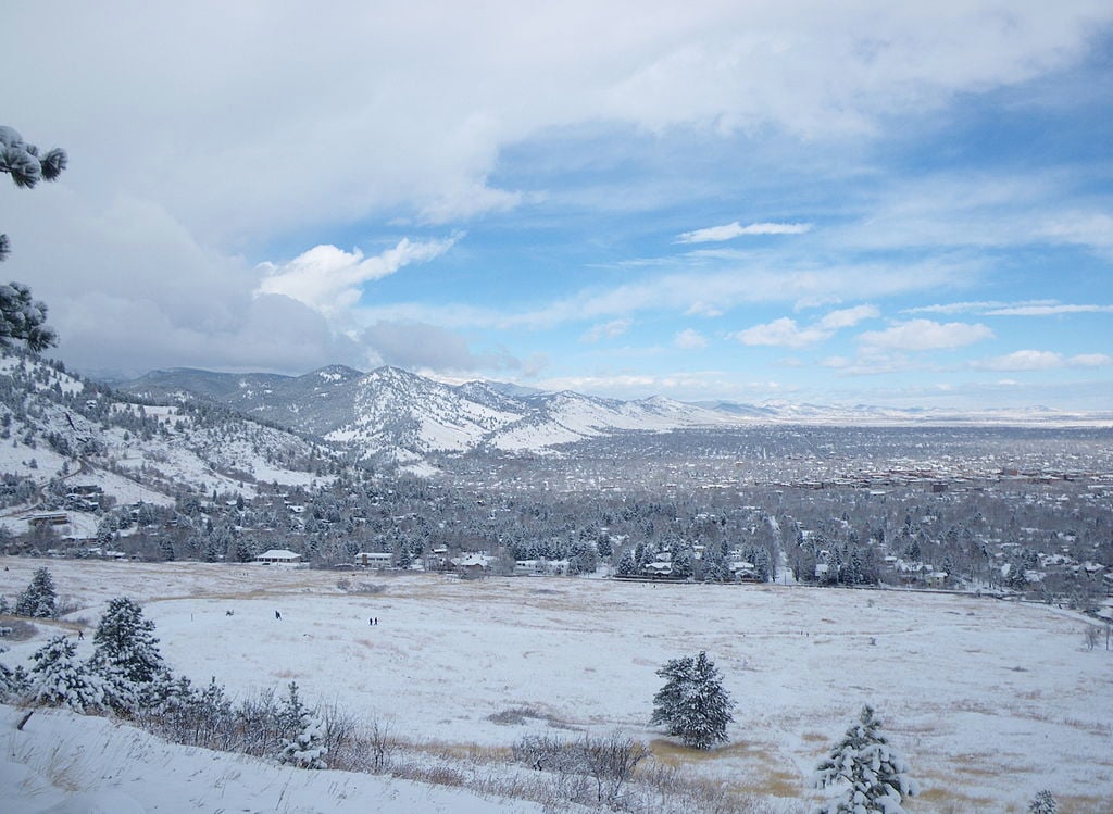 Snow-covered Boulder landscape with mountains and trees under a partly cloudy sky