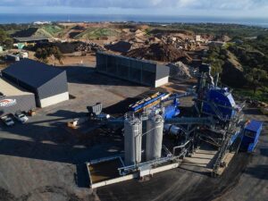 Aerial view of an asphalt production facility with blue equipment, storage silos, and aggregate stockpiles at a COLAS Australia site.