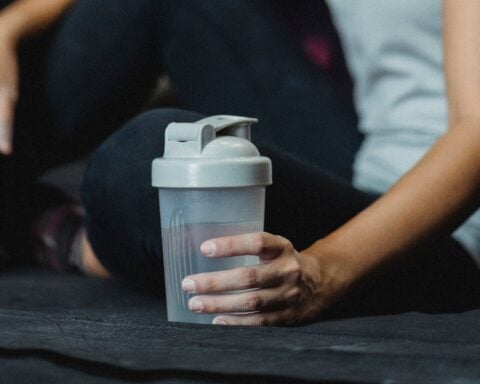 person in athletic wear holding a shaker bottle while seated on dark gym surface