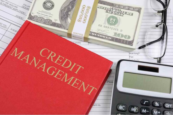 Red “Credit Management” book with calculator, glasses, hundred-dollar bills, and financial paperwork — symbolizing personal finance monitoring and credit score protection.