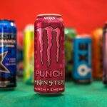 Cans of various energy drinks lined up on a table against a red and green background.