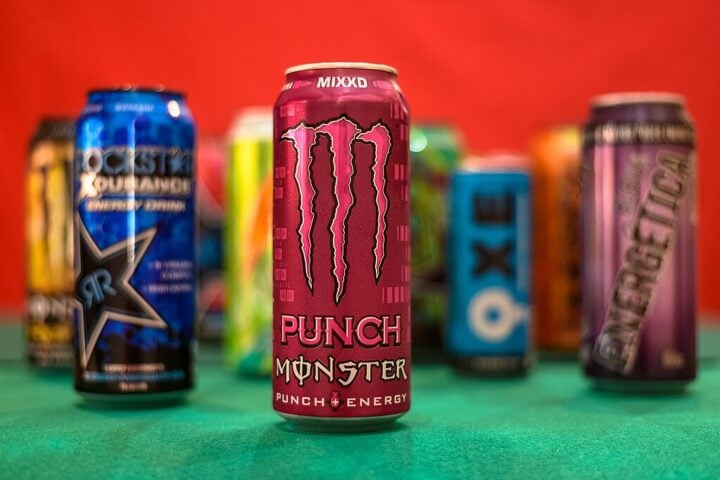Cans of various energy drinks lined up on a table against a red and green background.