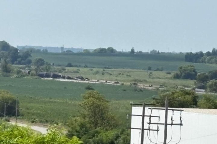 Train derailment near Reeseville, Wisconsin, showing several freight cars off the tracks in a rural landscape with fields and trees, with utility poles and wires in the foreground.