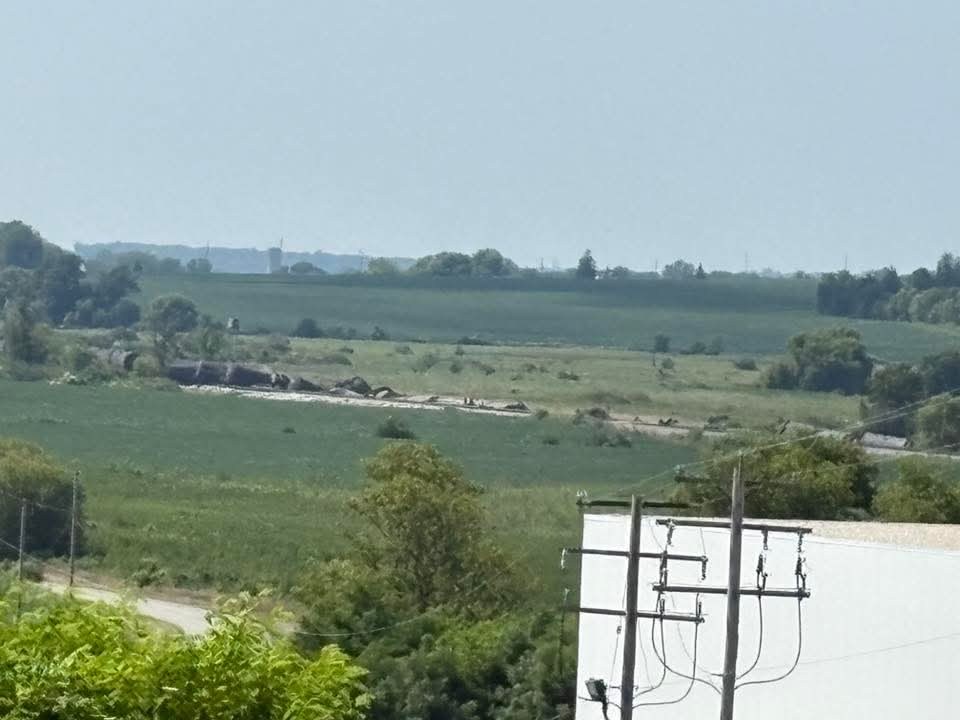 Train derailment near Reeseville, Wisconsin, showing several freight cars off the tracks in a rural landscape with fields and trees, with utility poles and wires in the foreground.