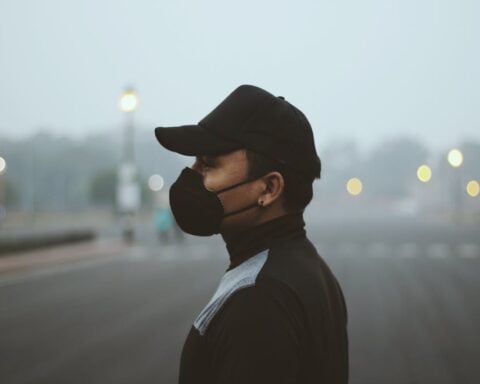 Side profile of a person wearing a protective mask standing outdoors in heavy haze.
