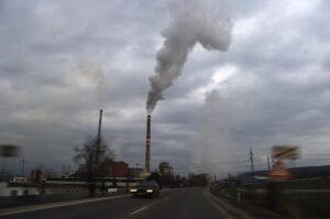 Industrial smokestacks emitting dark pollution into a cloudy sky over an urban area, illustrating air pollution from industrial facilities.