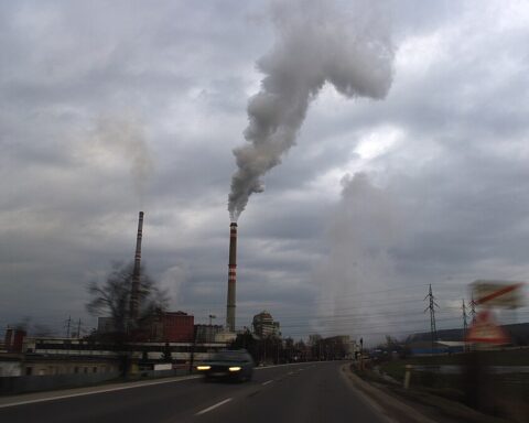 Industrial smokestacks emitting dark pollution into a cloudy sky over an urban area, illustrating air pollution from industrial facilities.