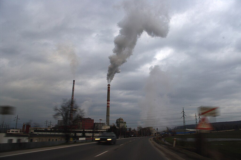Industrial smokestacks emitting dark pollution into a cloudy sky over an urban area, illustrating air pollution from industrial facilities.