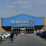 Exterior of a Walmart Supercentre store with blue and yellow signage, parked cars in the foreground, and shoppers walking toward the entrance.