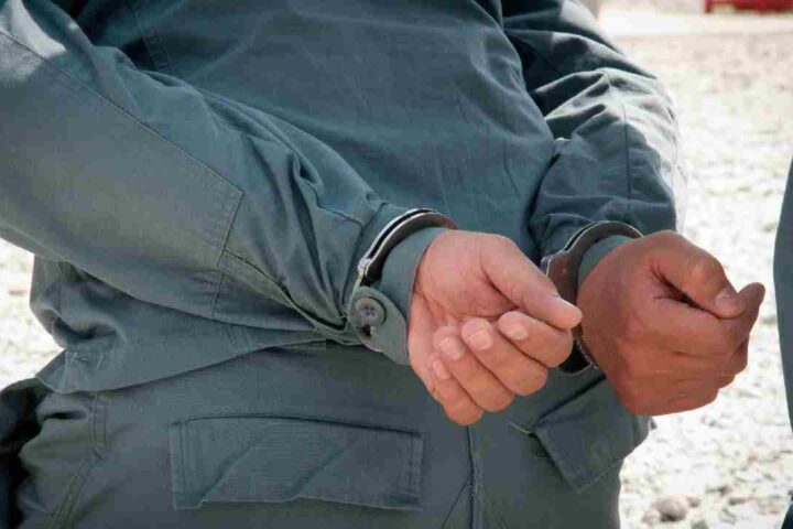 A person’s hands secured in metal handcuffs behind their back.