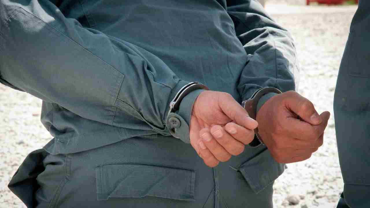 A person’s hands secured in metal handcuffs behind their back.