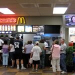Busy fast-food drive‑thru at night in a city, with multiple cars in line and illuminated menu boards.