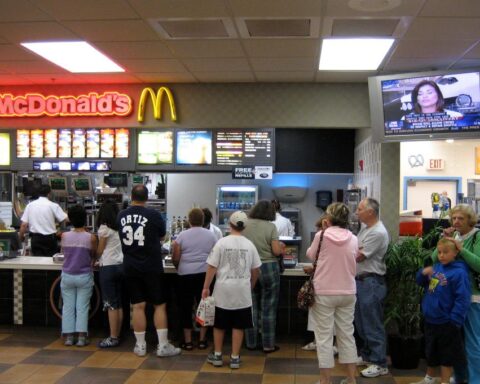 Busy fast-food drive‑thru at night in a city, with multiple cars in line and illuminated menu boards.