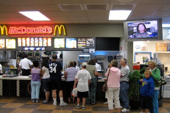 Busy fast-food drive‑thru at night in a city, with multiple cars in line and illuminated menu boards.