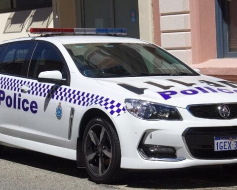 White Western Australia Police–branded Holden Commodore VF II SV6 Sportwagon parked outside a historic sandstone building, showing its blue-and-white chequered livery and emergency lightbar.