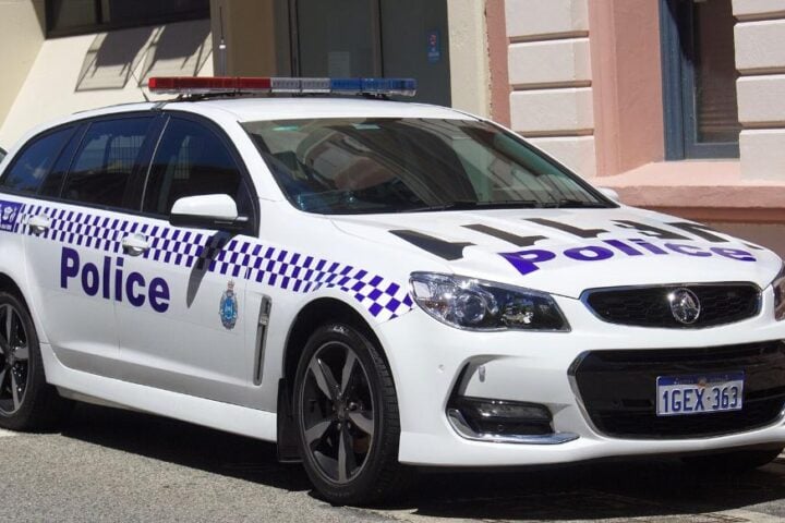 White Western Australia Police–branded Holden Commodore VF II SV6 Sportwagon parked outside a historic sandstone building, showing its blue-and-white chequered livery and emergency lightbar.