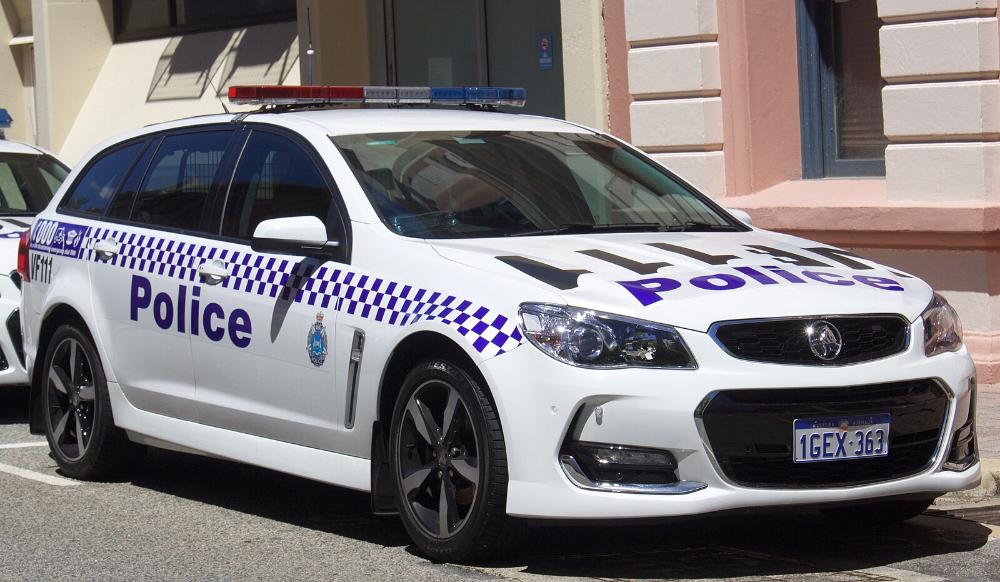 White Western Australia Police–branded Holden Commodore VF II SV6 Sportwagon parked outside a historic sandstone building, showing its blue-and-white chequered livery and emergency lightbar.