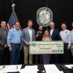 Group of people standing with ceremonial check in front of American and Florida flags, celebrating Florida Python Challenge grand prize winner