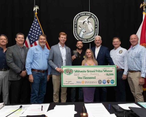 Group of people standing with ceremonial check in front of American and Florida flags, celebrating Florida Python Challenge grand prize winner