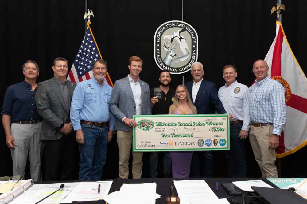Group of people standing with ceremonial check in front of American and Florida flags, celebrating Florida Python Challenge grand prize winner